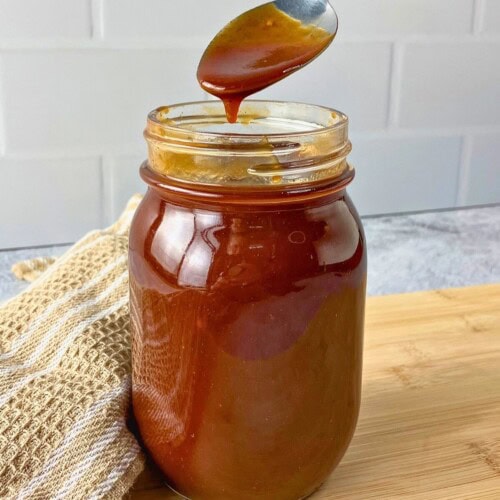 Homemade BBQ sauce in a jar with some dripping off a spoon back into the jar.
