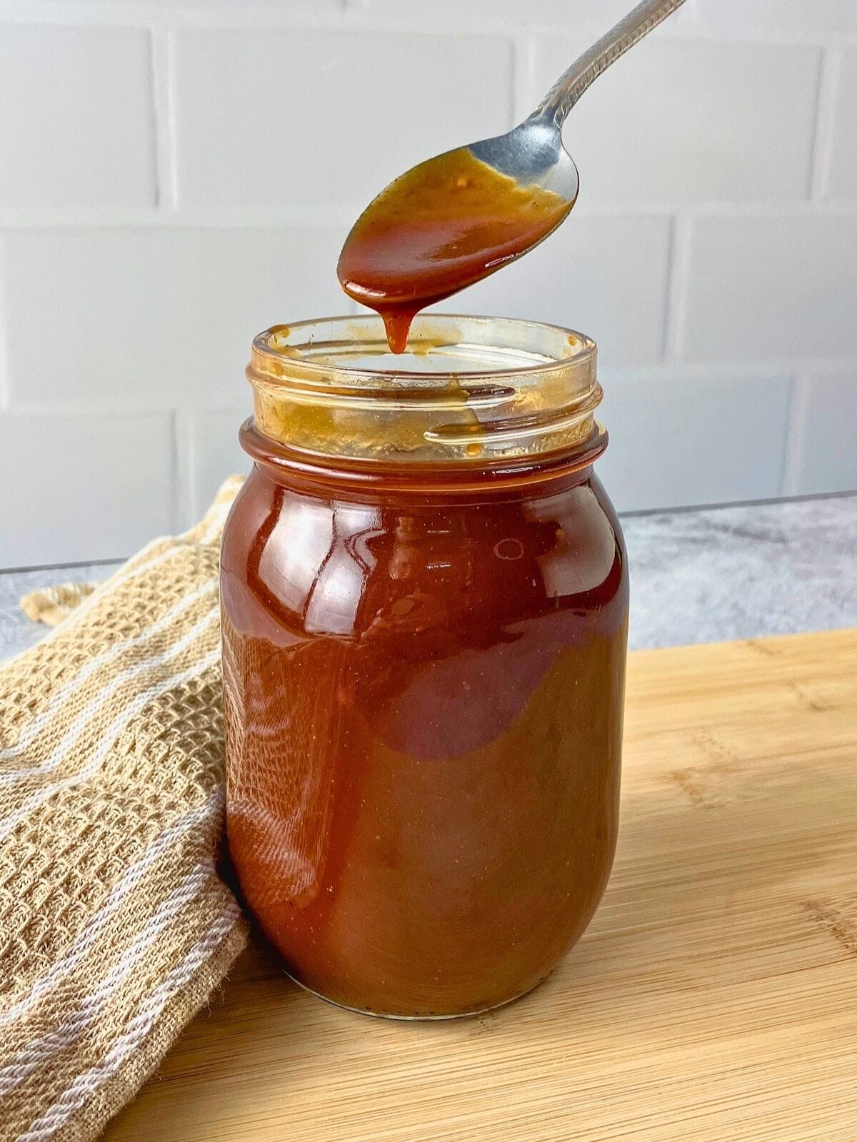 Homemade BBQ sauce in a jar with some dripping off a spoon back into the jar.