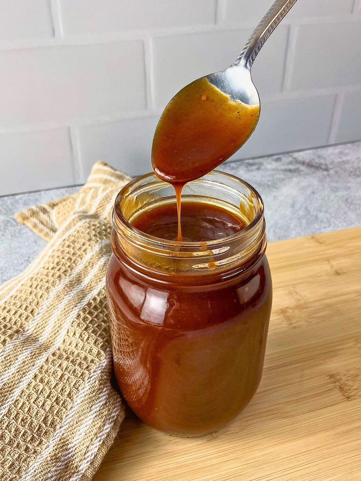 Homemade BBQ sauce in a jar with a spoon drizzling some back into the jar.