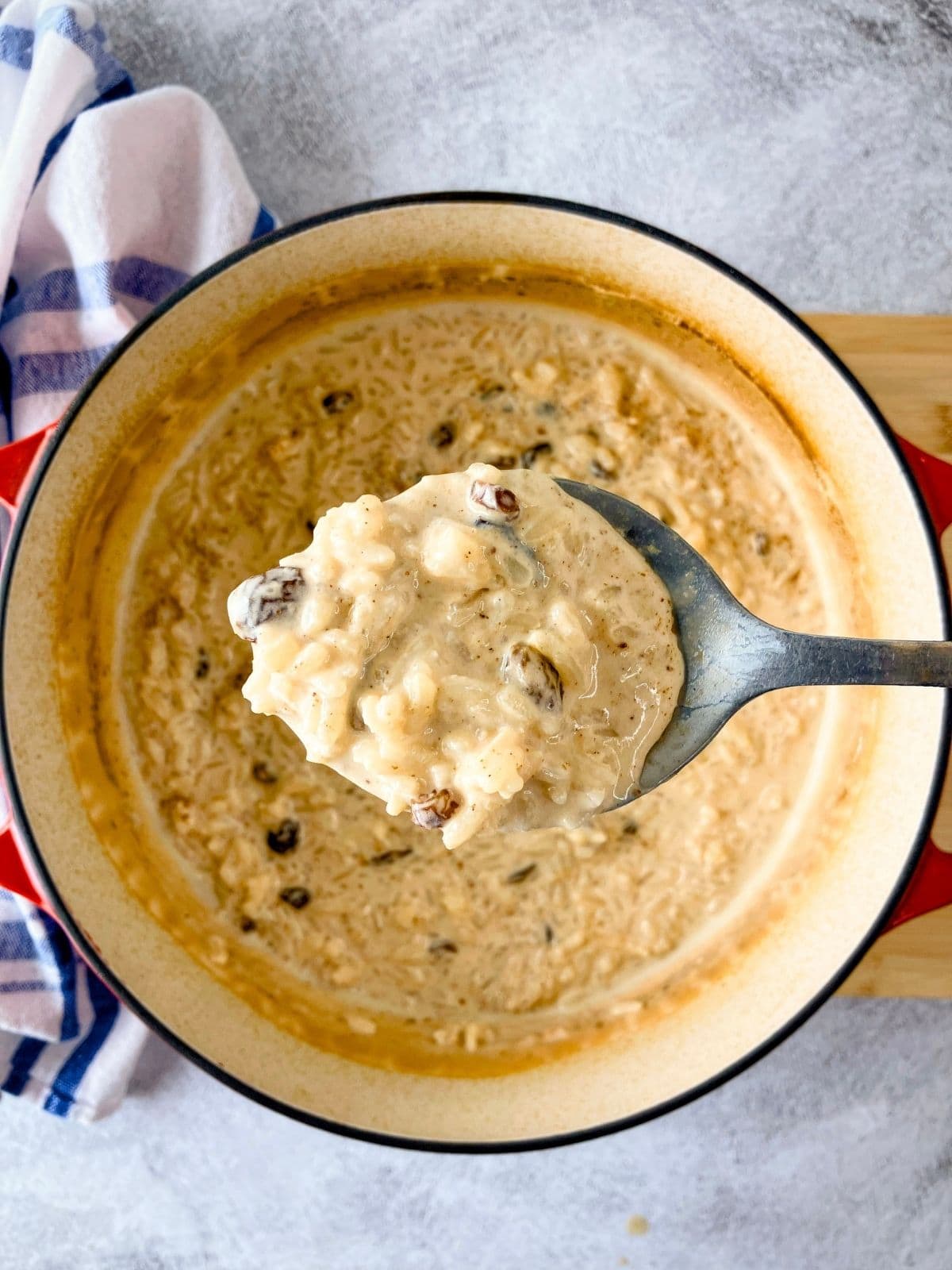 Lifting up a serving spoon of baked rice pudding over the pot.