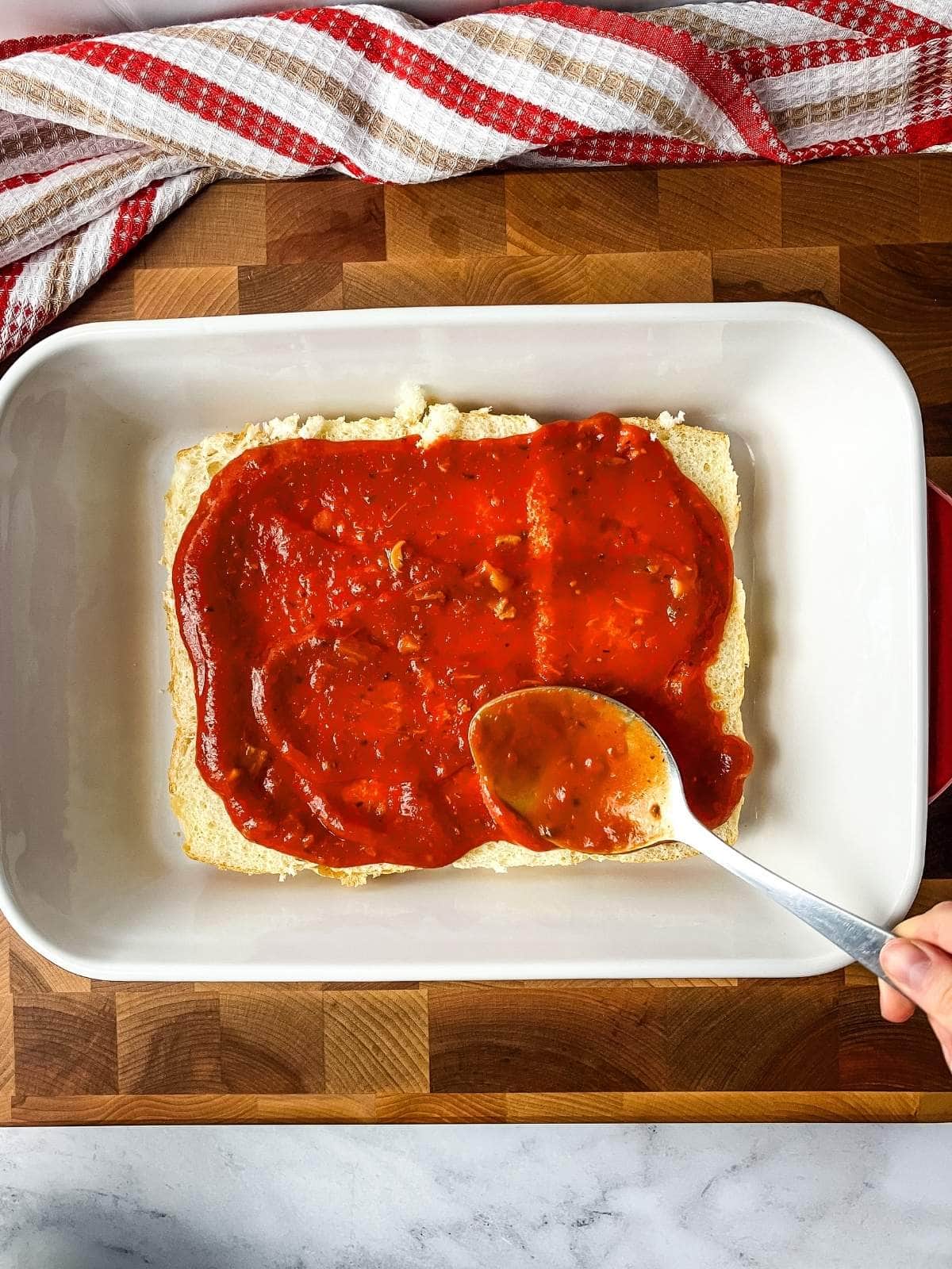 Spreading the tomato sauce over the bottom layer of rolls.