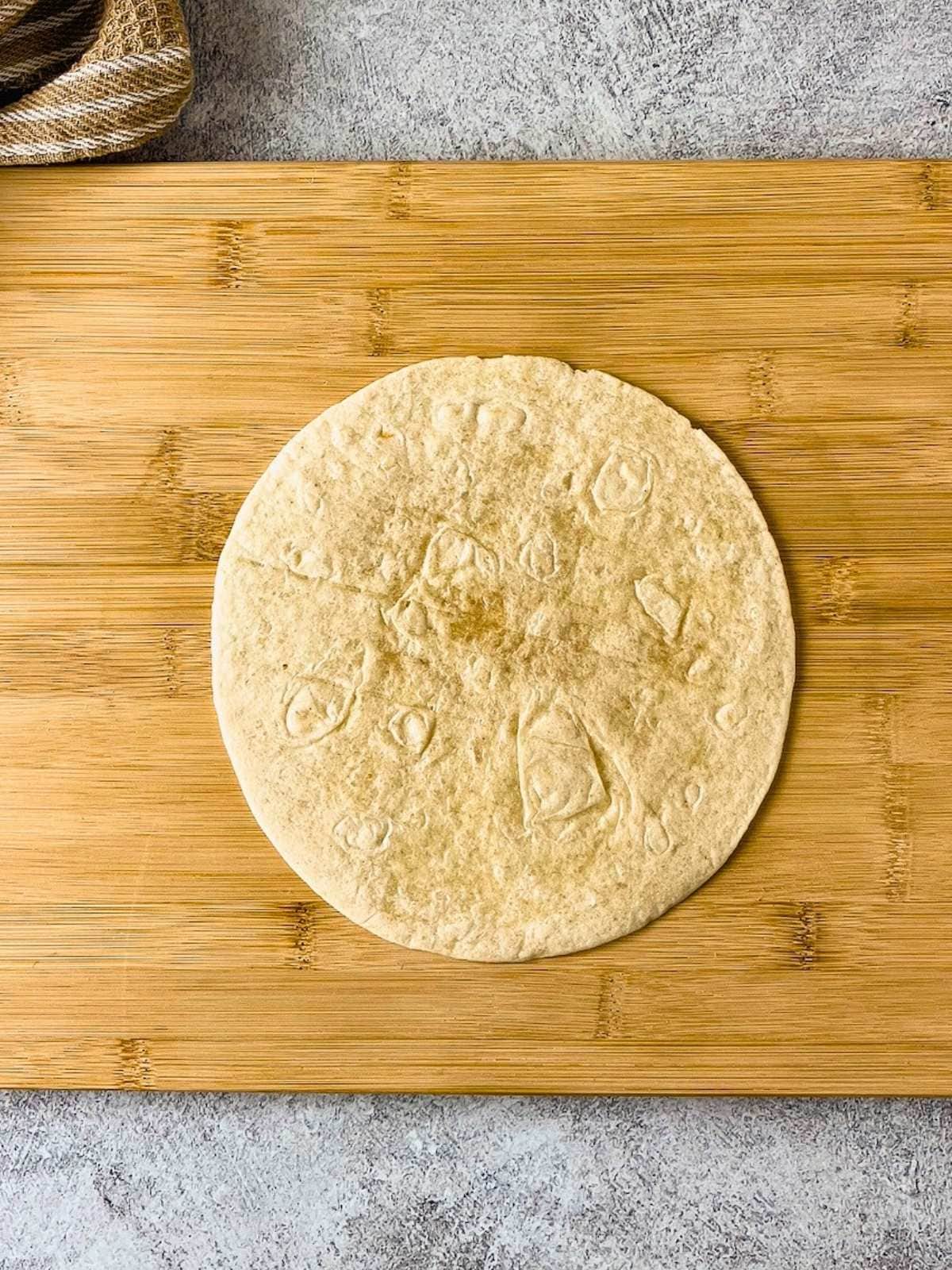 A flour tortilla on a cutting board.