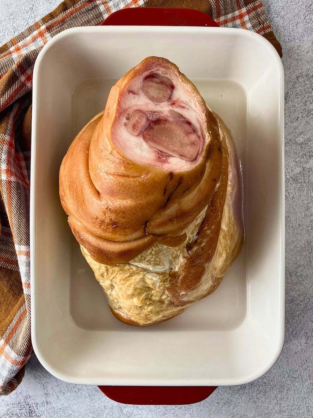 A bone in ham in a baking dish with water added.