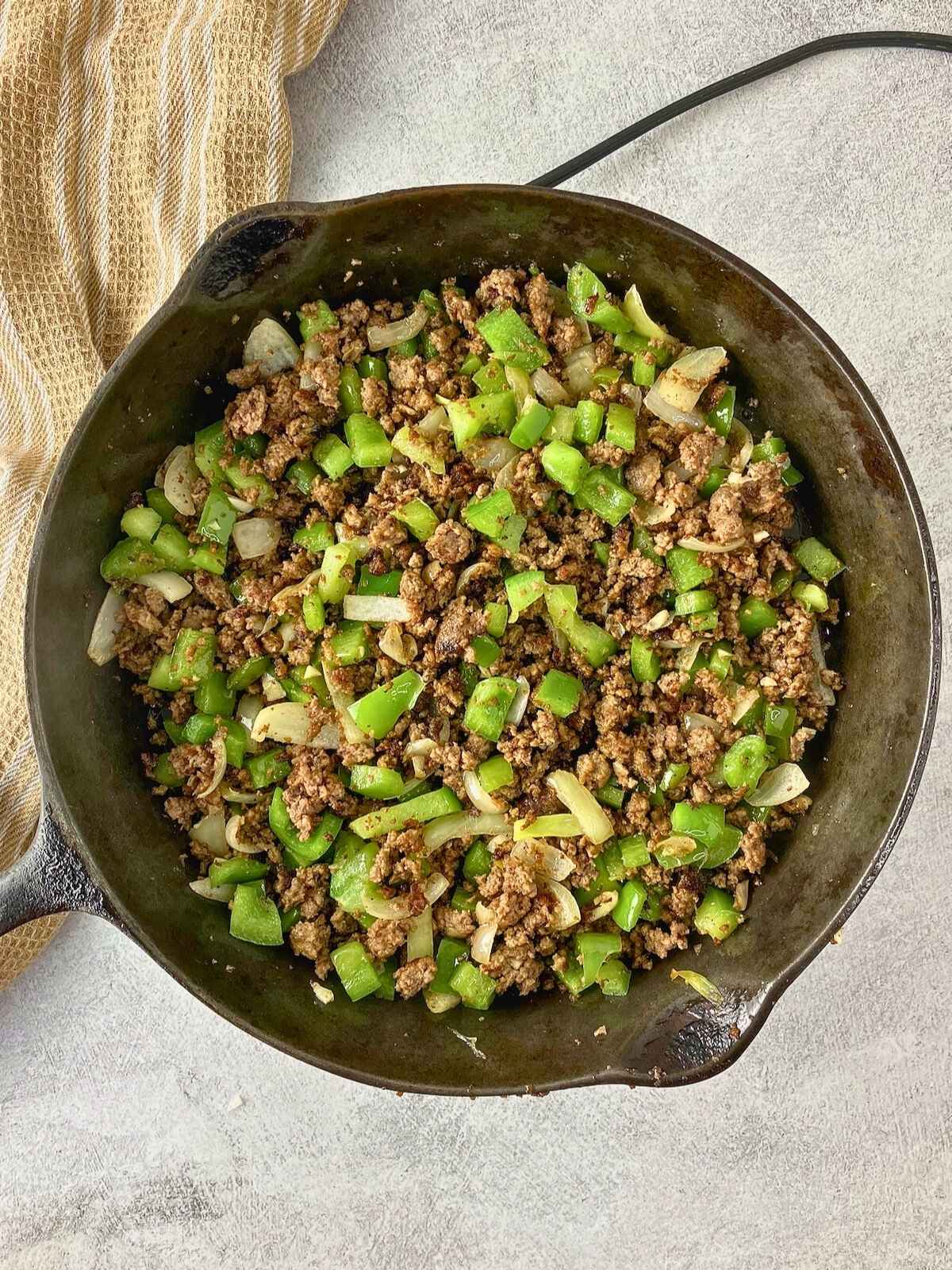 Cooked ground beef, onions, garlic, and peppers cooked in a cast iron skillet.