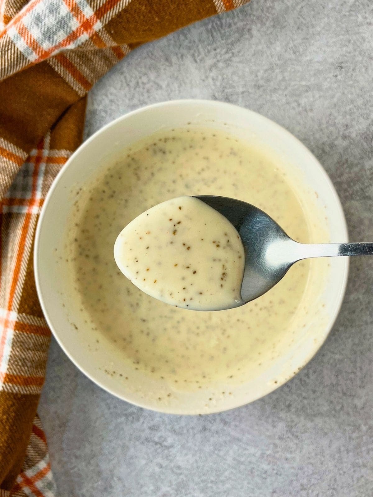 Holding some of the homemade coleslaw dressing up on a spoon above the bowl.