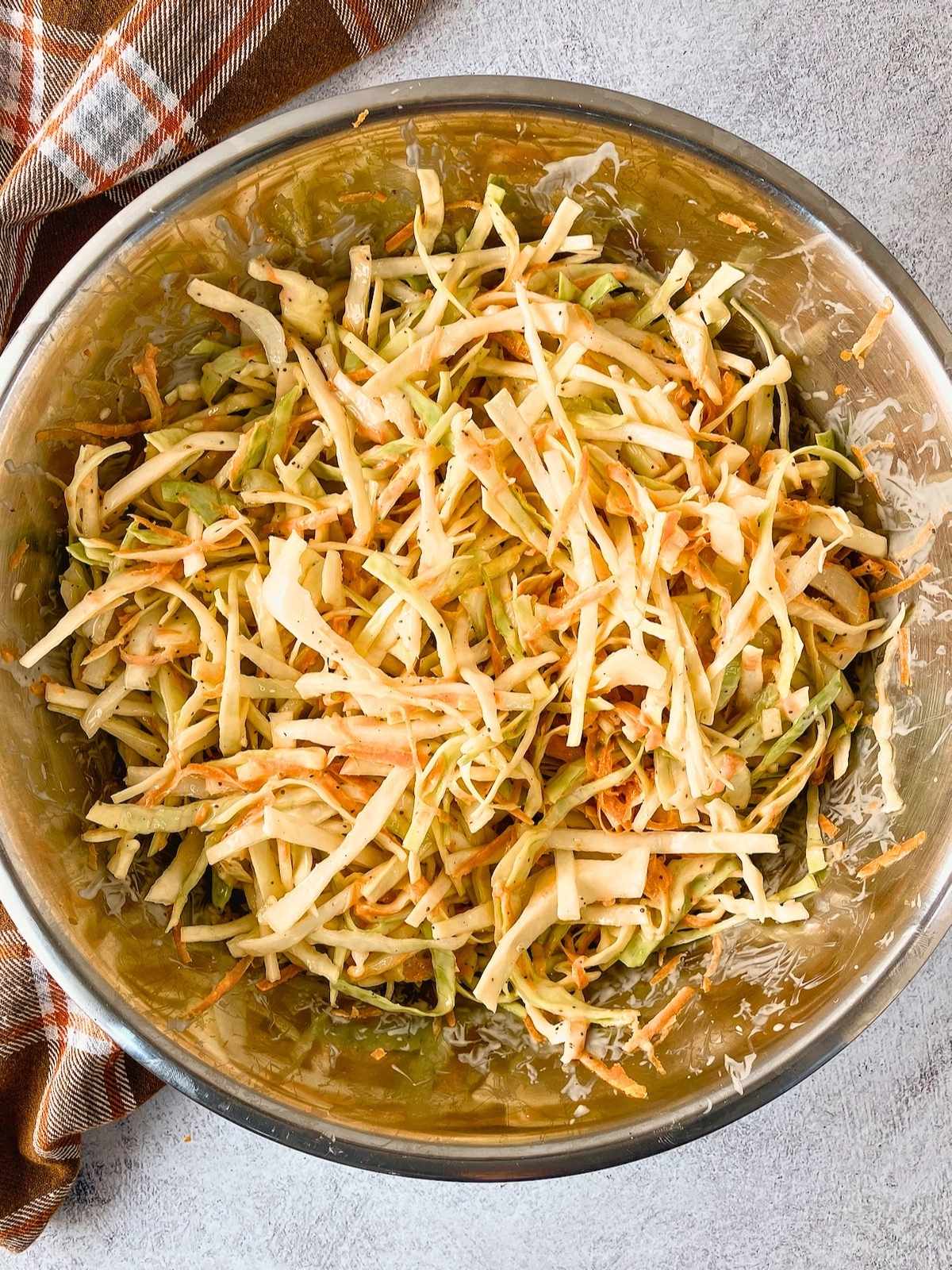A large steel mixing bowl of homemade coleslaw after mixing.