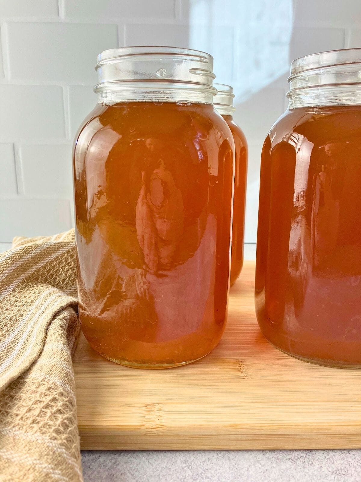 Quart jars filled with vegetable broth are sitting on a wooden cutting board on the counter.