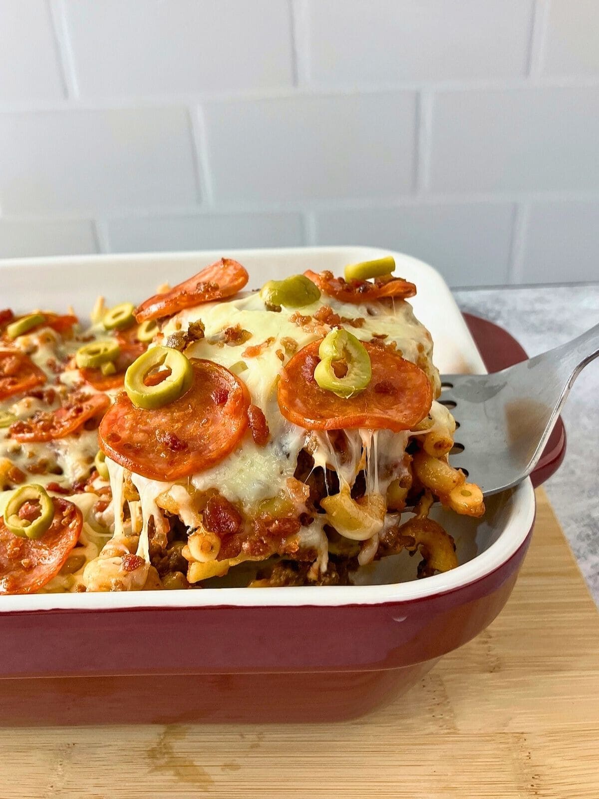 Lifting a serving of pizza pasta casserole out of the baking dish.