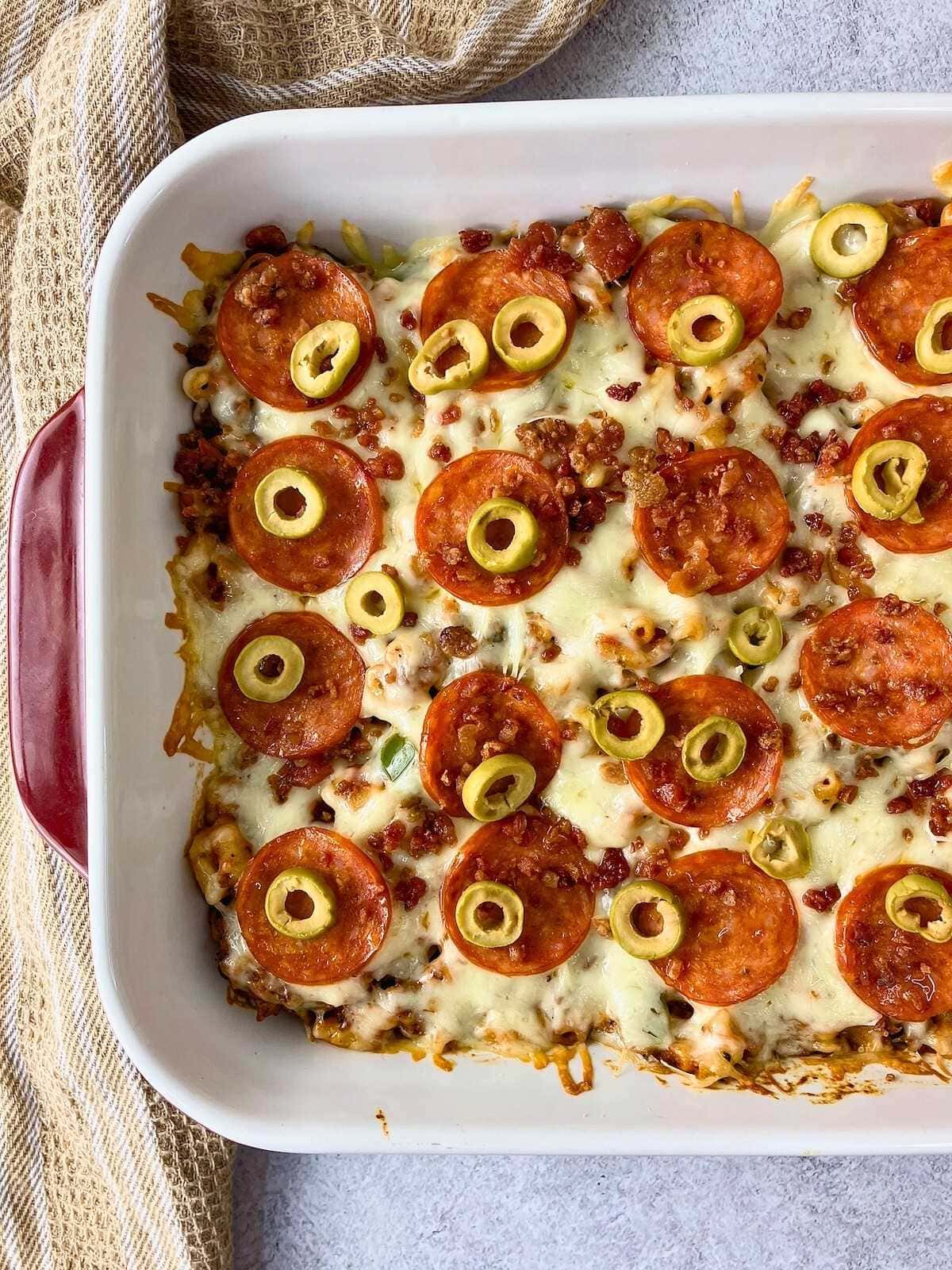 A red and white casserole dish of pizza bake casserole cooling on the counter.
