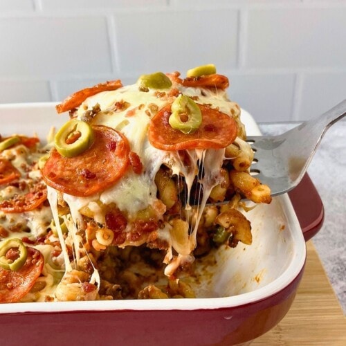 Pizza pasta casserole in a baking dish with a serving being lifted out.