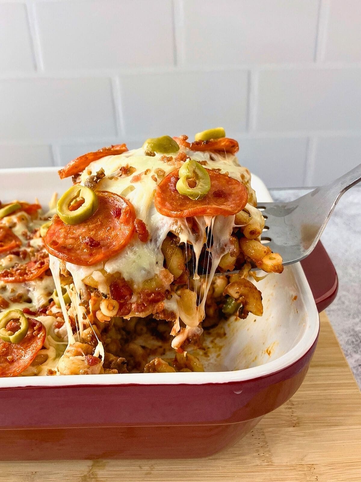 Pizza pasta casserole in a baking dish with a serving being lifted out.