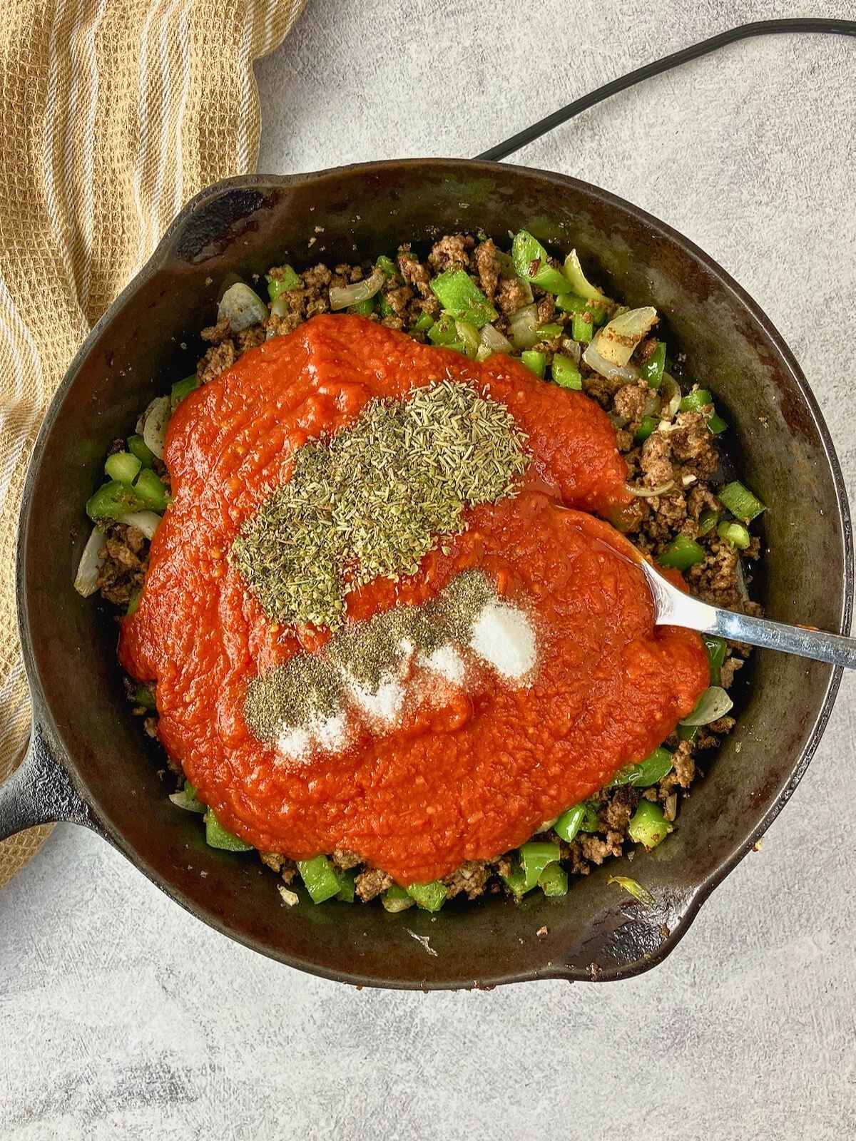 Tomato sauce and seasonings were added to the meat and vegetable mixture in the frying pan.