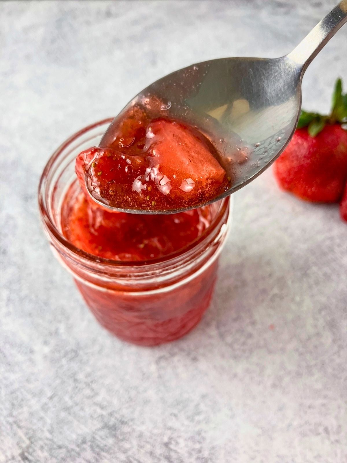 A spoonful of fresh homemade strawberry jam is held over an open jar.