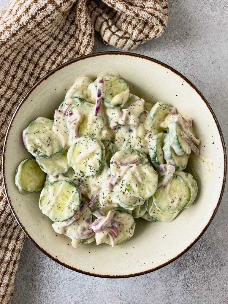 A serving bowl of creamy cucumber salad with red onions and dill dressing.