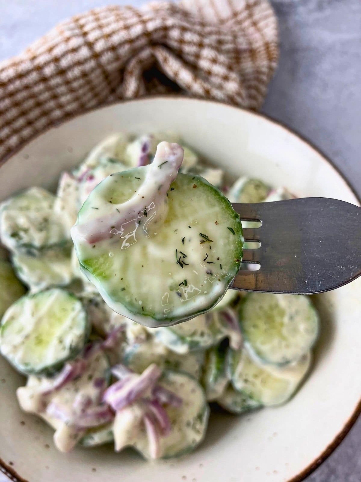 Homemade creamy cucumber salad in a brown serving bowl with a forkful lifted up.