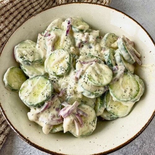 Homemade creamy cucumber salad in a brown serving bowl.