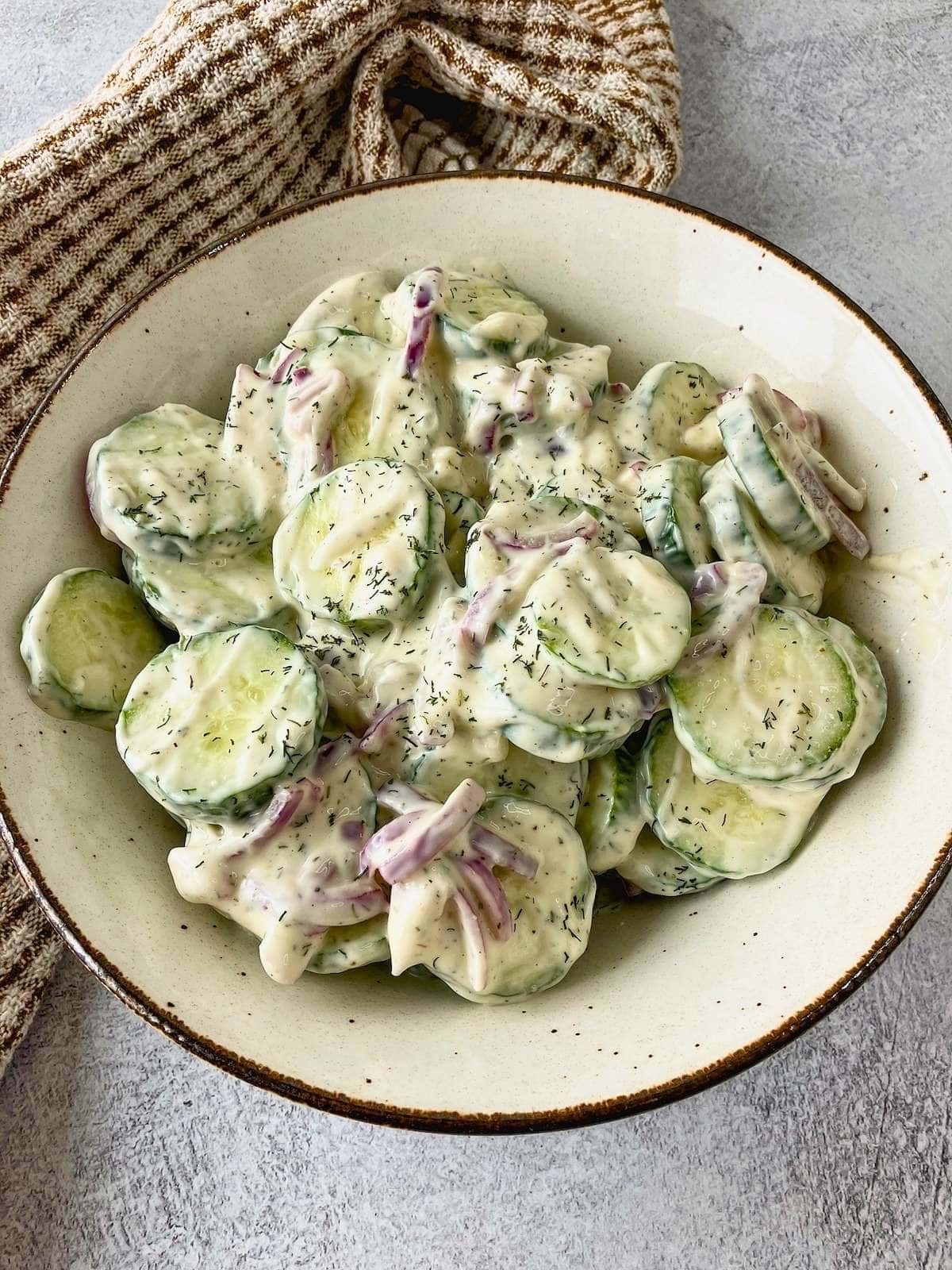 Homemade creamy cucumber salad in a brown serving bowl.