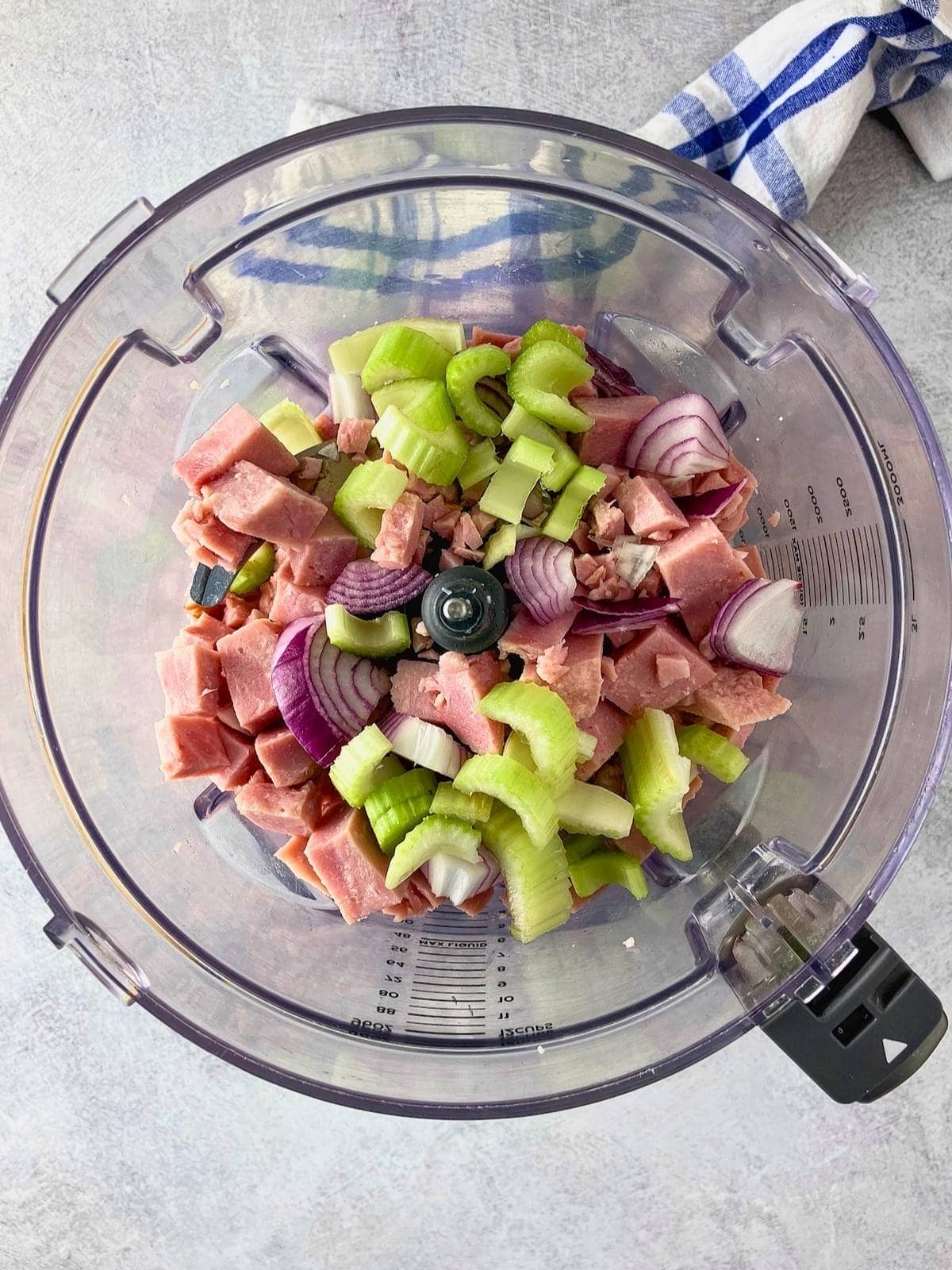 Diced ham, celery, and red onion in a food processor bowl.