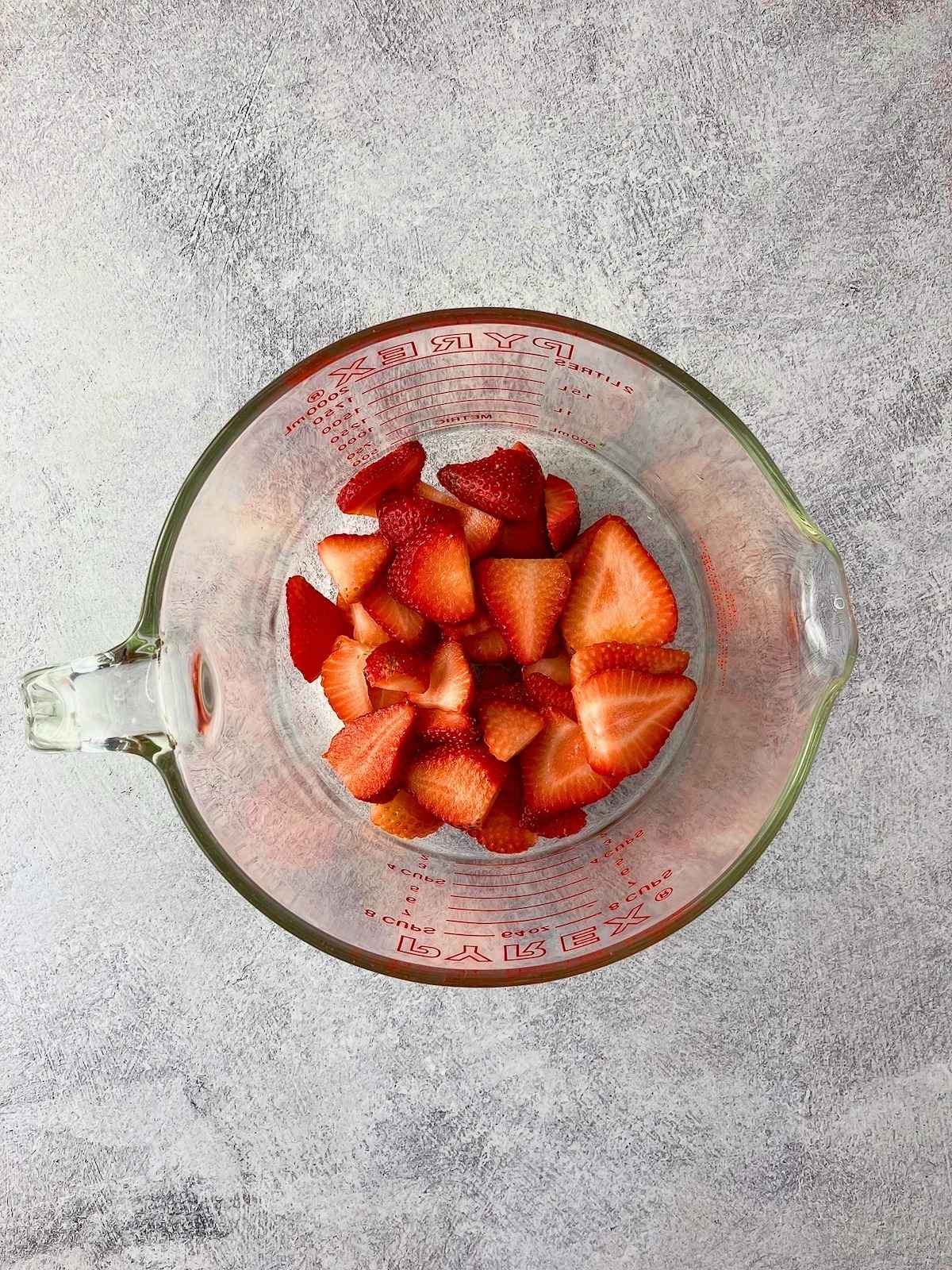 A layer of sliced strawberries in a measuring cup.