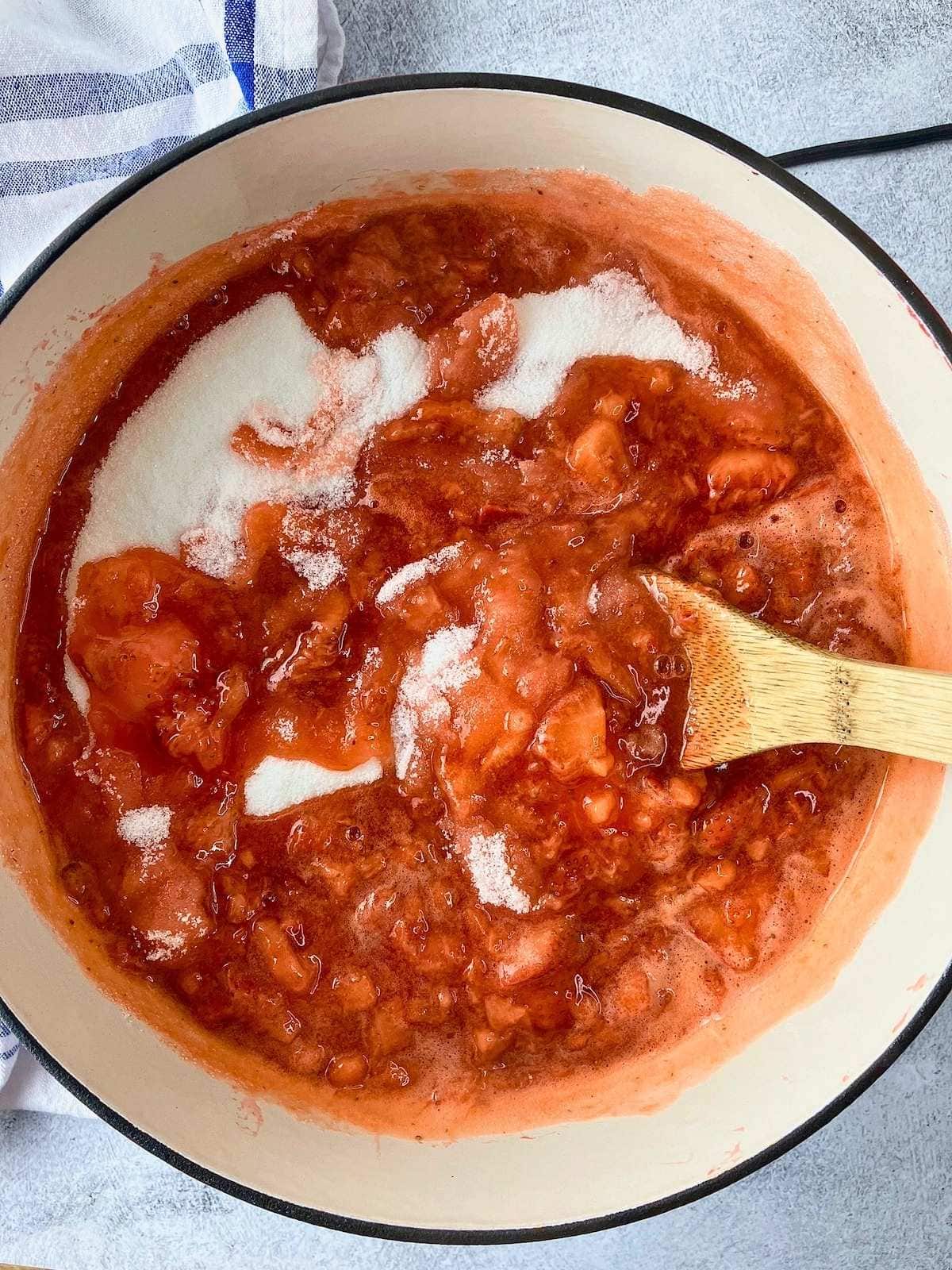 Stirring the sugar into the hot strawberries until it dissolves.