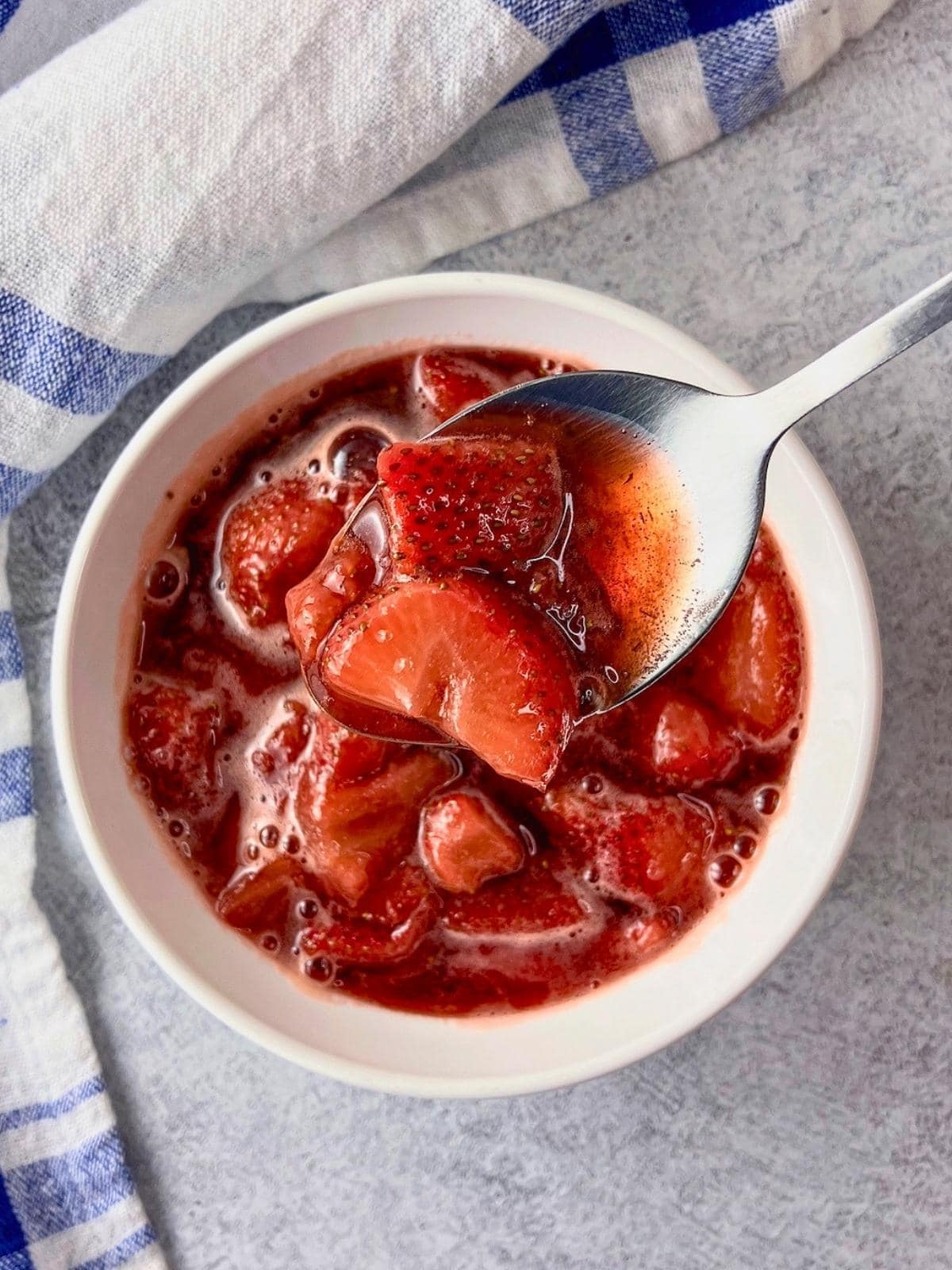 Lifting a spoonful of strawberry compote up over a white serving bowl.