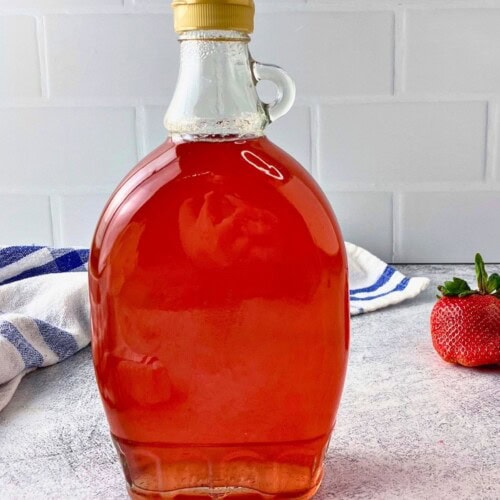 A bottle of homemade strawberry top syrup is on the counter next to fresh strawberries.
