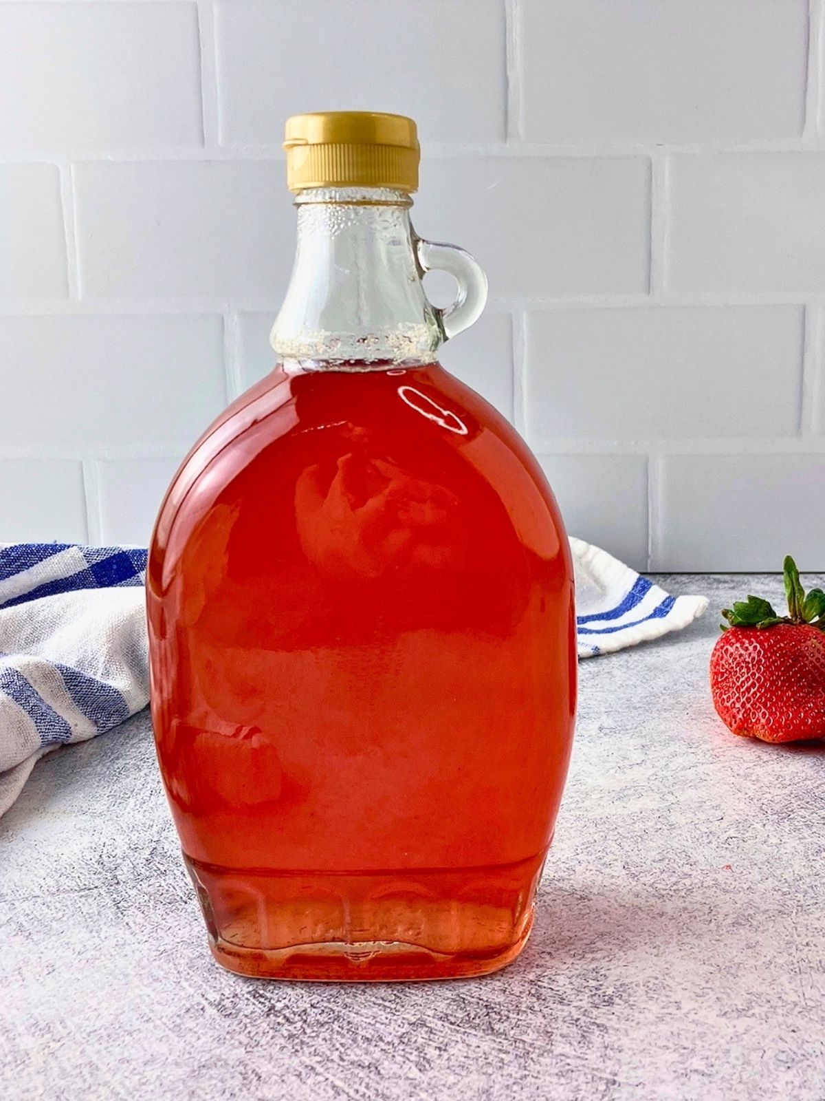 A bottle of homemade strawberry top syrup is on the counter next to fresh strawberries.