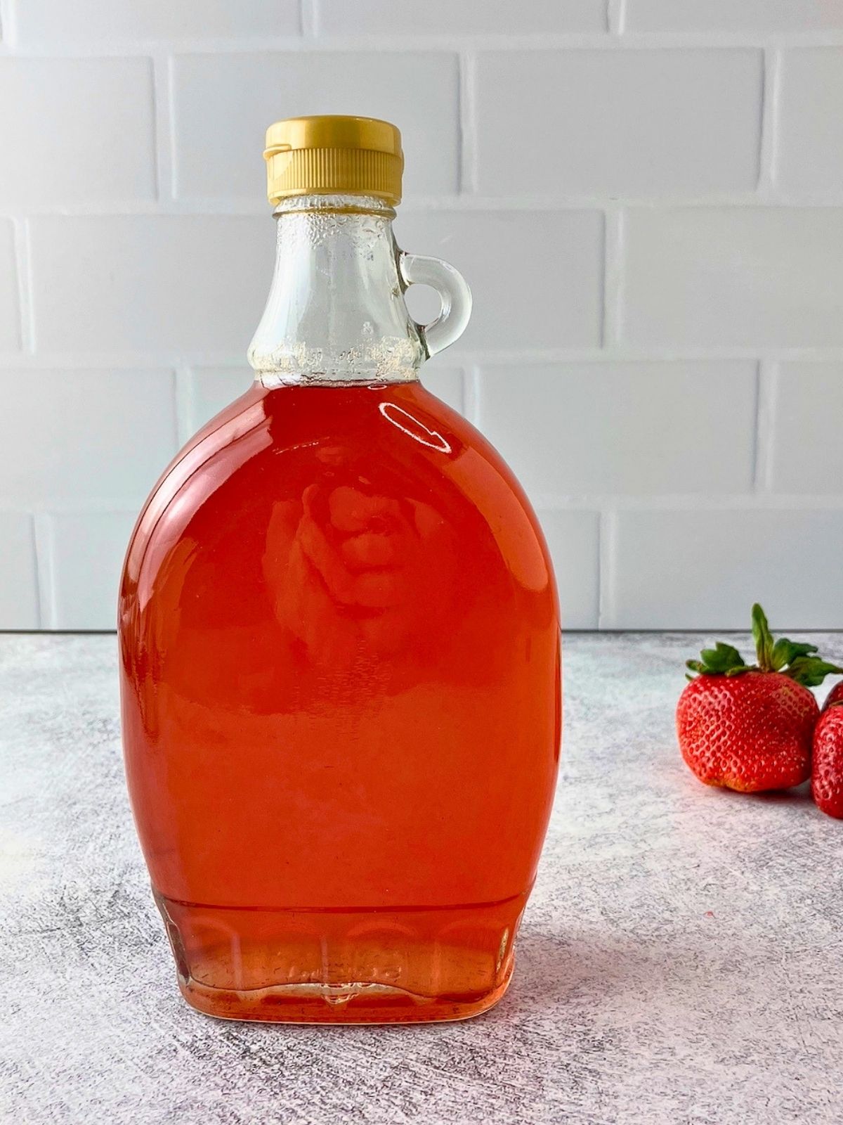 A bottle of homemade strawberry top syrup is on the counter next to fresh strawberries.