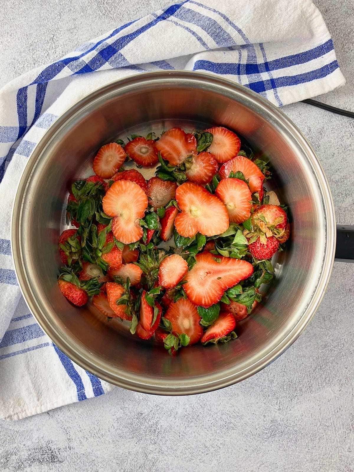 The strawberry tops with leaves were added to a medium saucepan.