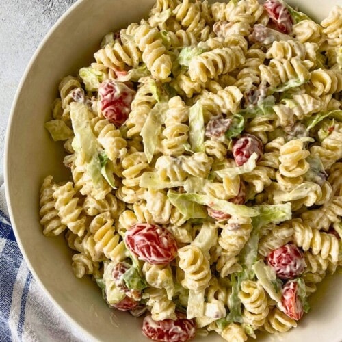 Creamy BLT pasta salad with rotini, grape tomatoes, lettuce, and bacon pieces served in a white bowl on a gray countertop.