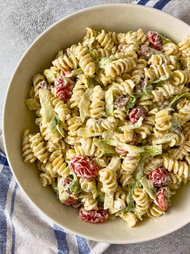 Creamy BLT pasta salad with rotini, grape tomatoes, lettuce, and bacon pieces served in a white bowl on a gray countertop.
