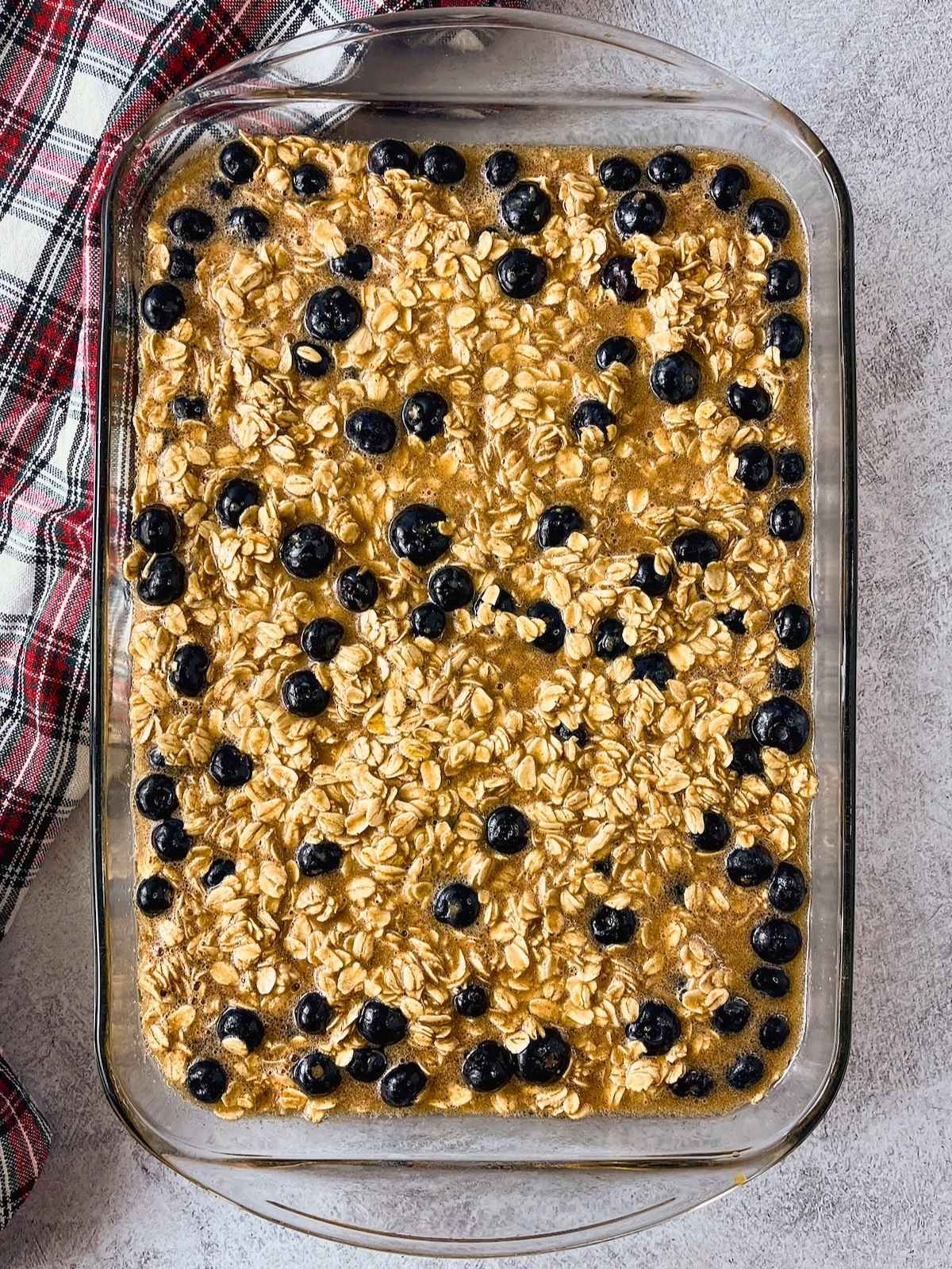 Unbaked blueberry baked oatmeal mixture in a glass baking dish, with oats and whole blueberries spread through the batter.