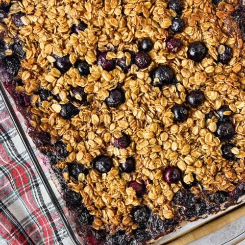 Glass baking dish filled with blueberry baked oatmeal, with golden oats and whole blueberries baked across the top.