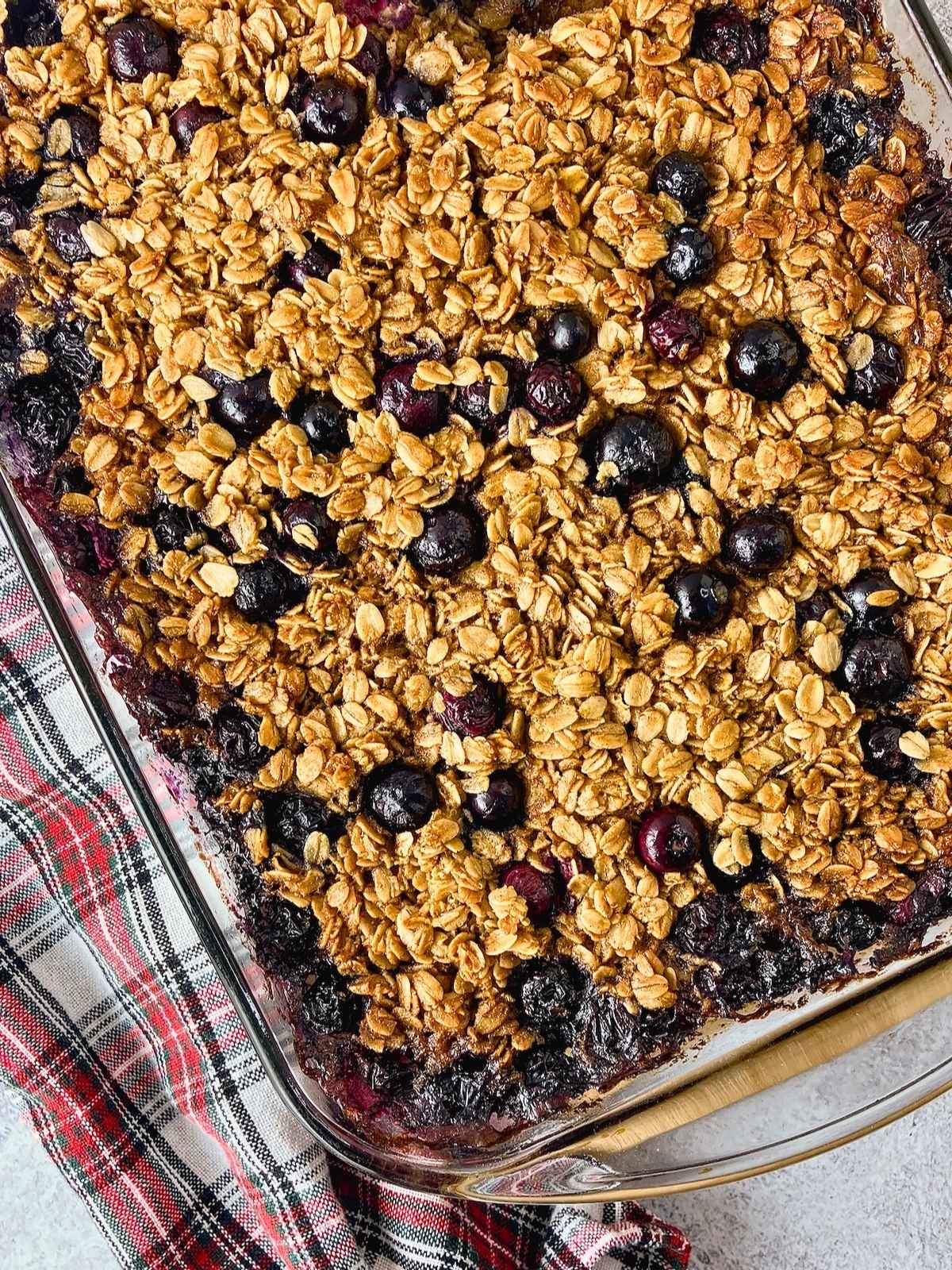 Glass baking dish filled with blueberry baked oatmeal, with golden oats and whole blueberries baked across the top.