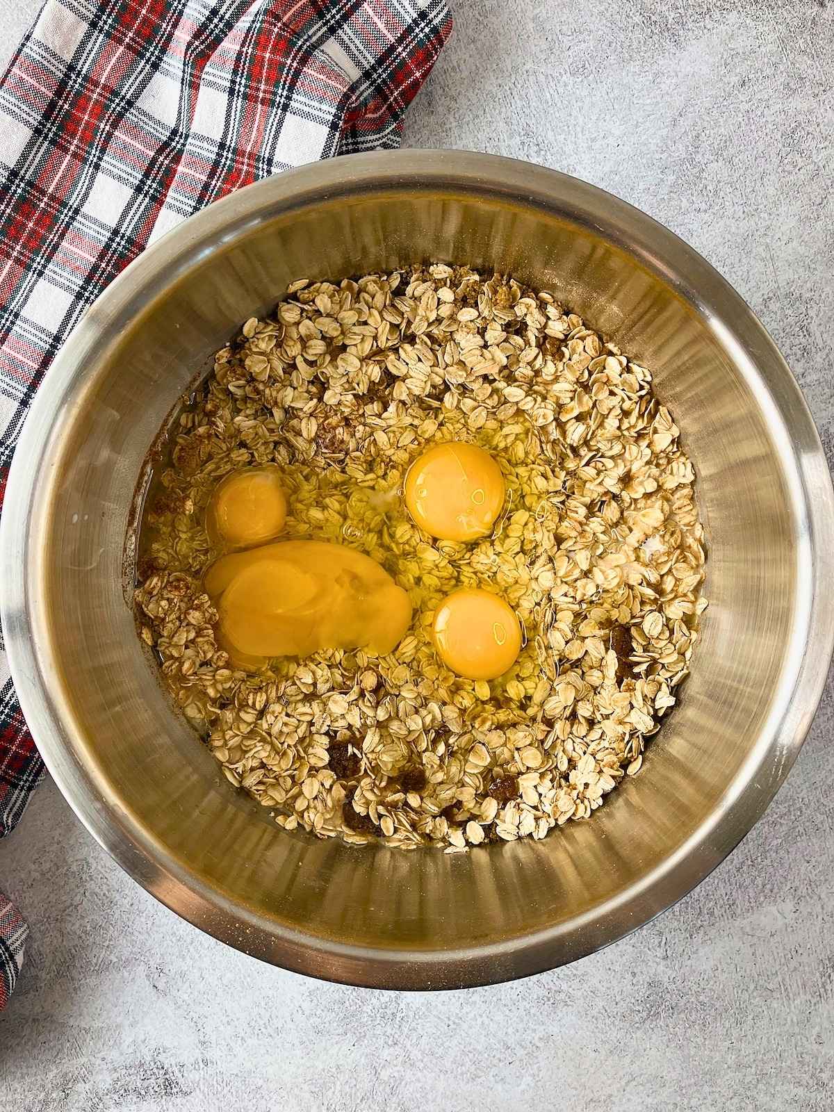 Mixing bowl with oats, eggs, oil, and brown sugar is ready to be stirred.