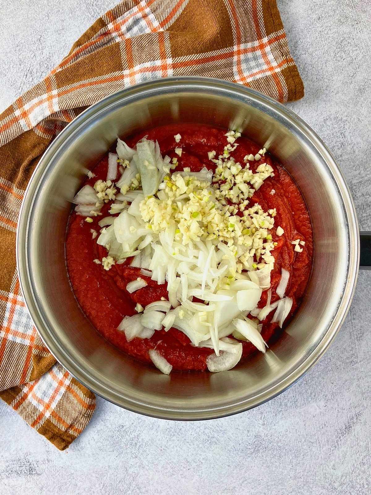 Pot with crushed tomatoes, chopped onion, and minced garlic.