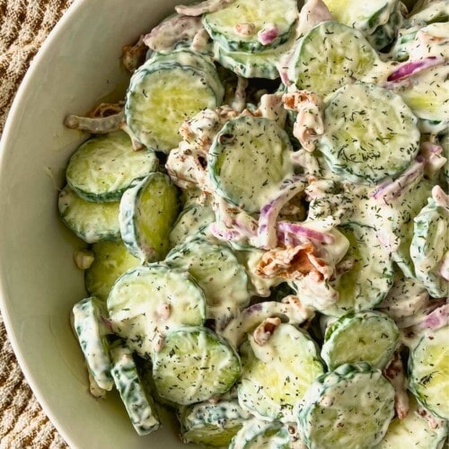 Creamy bacon cucumber salad with sliced cucumbers, red onion, bacon pieces, and dill in a white bowl.