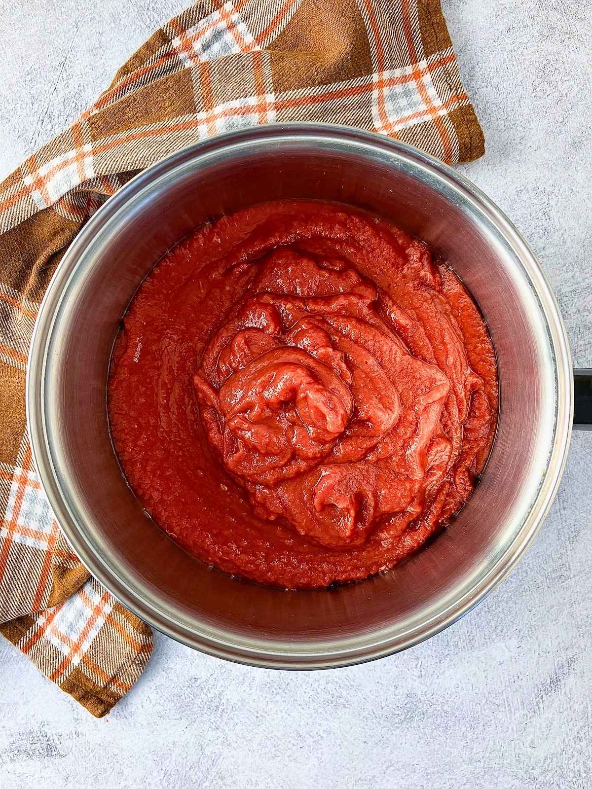Pot of crushed tomatoes with an orange plaid towel on the counter.