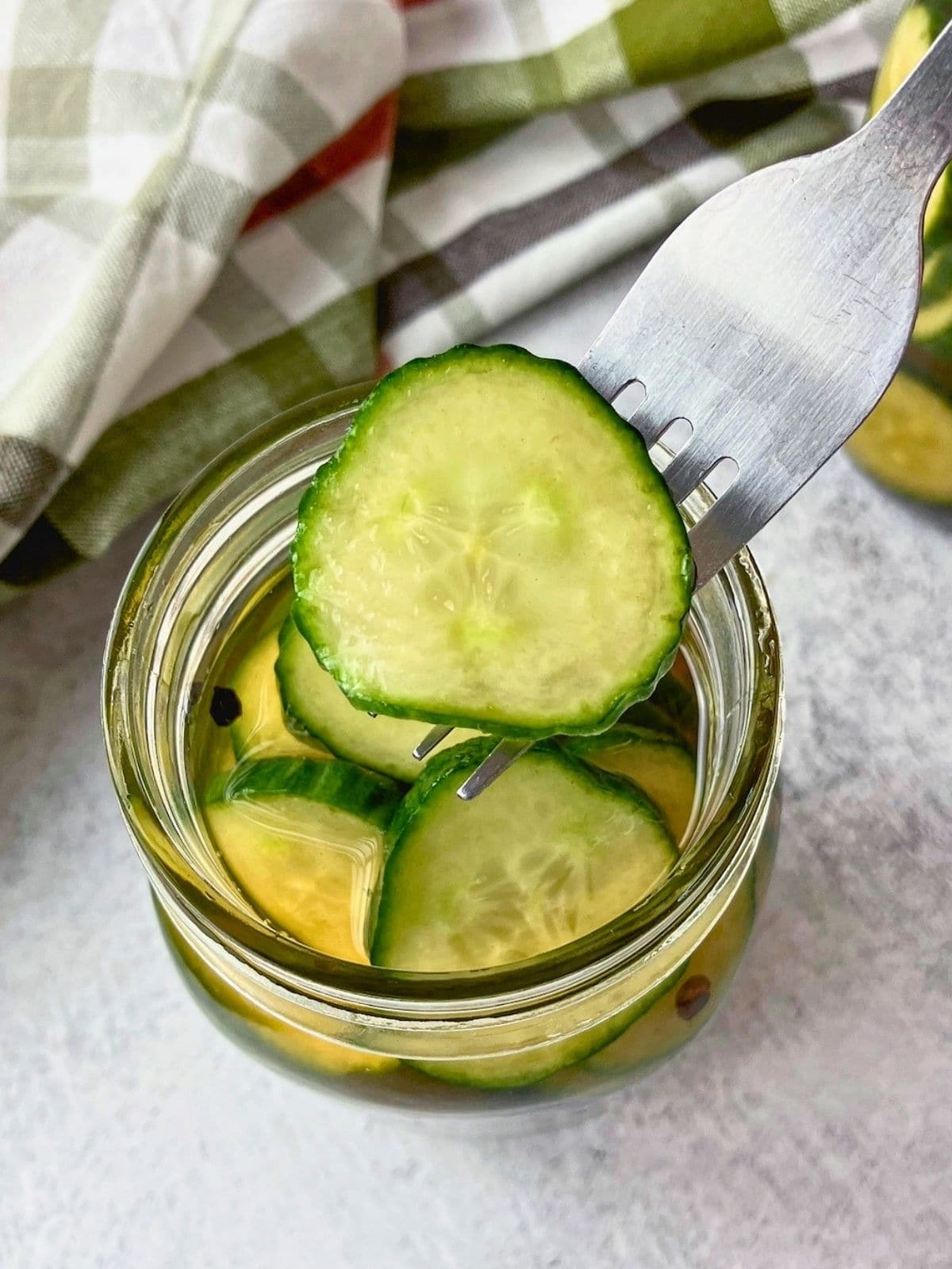 Fork lifting a sliced pickle from a glass jar filled with quick cucumber pickles.