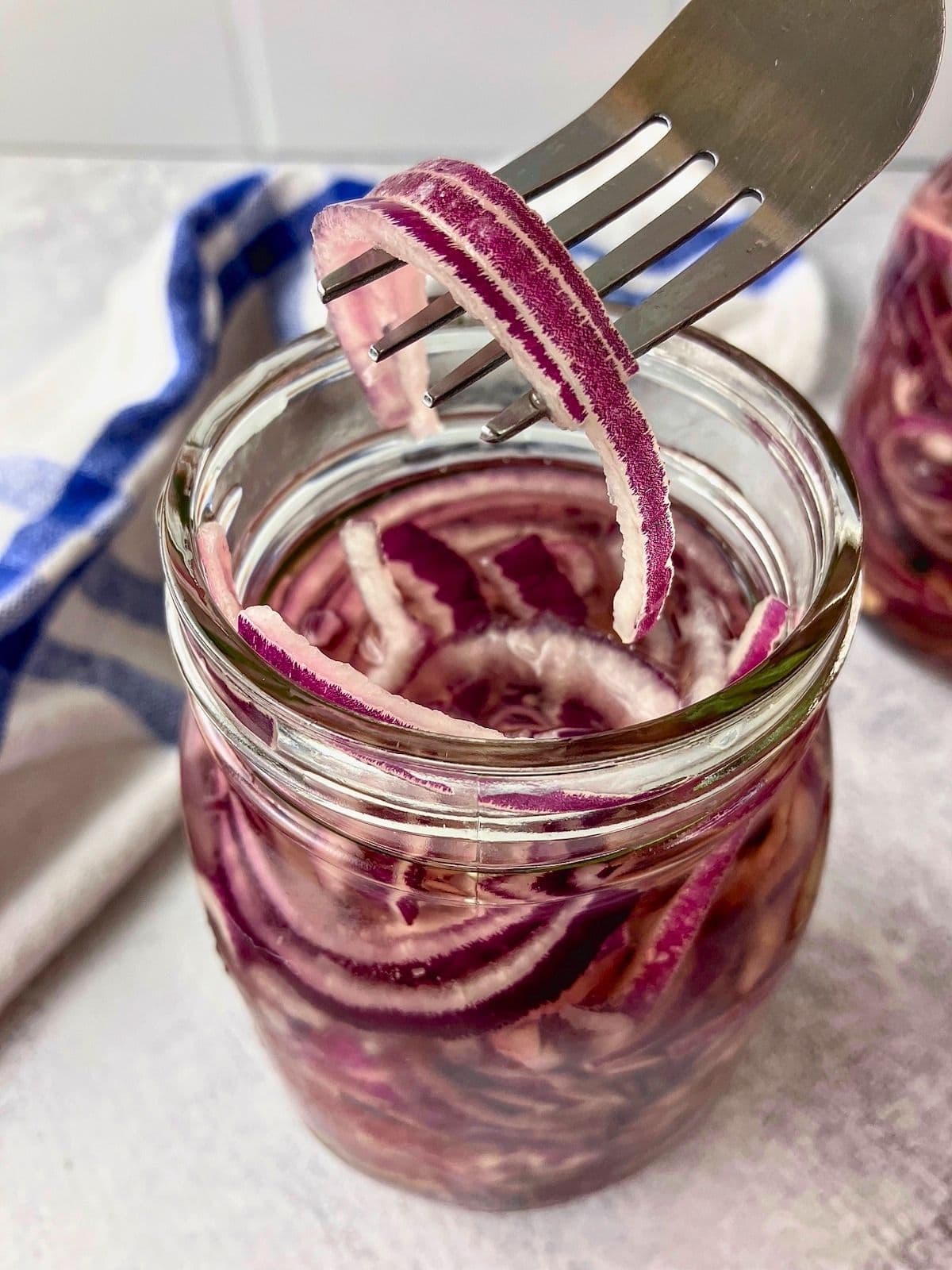 Fork lifting a thin slice of pickled red onion from a glass jar.