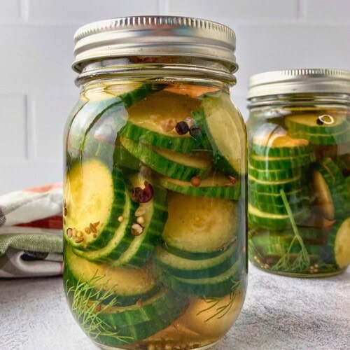 Two jars of refrigerator dill pickles with sliced cucumbers and dill in golden brine.