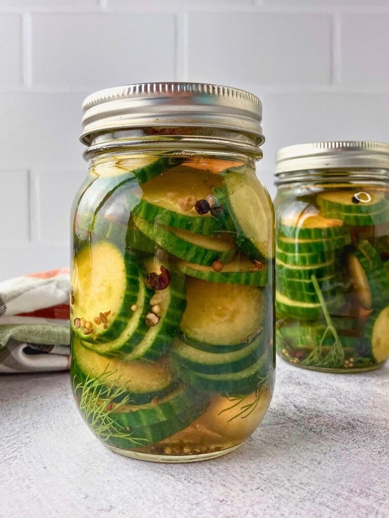 Two jars of refrigerator dill pickles with sliced cucumbers and dill in golden brine.