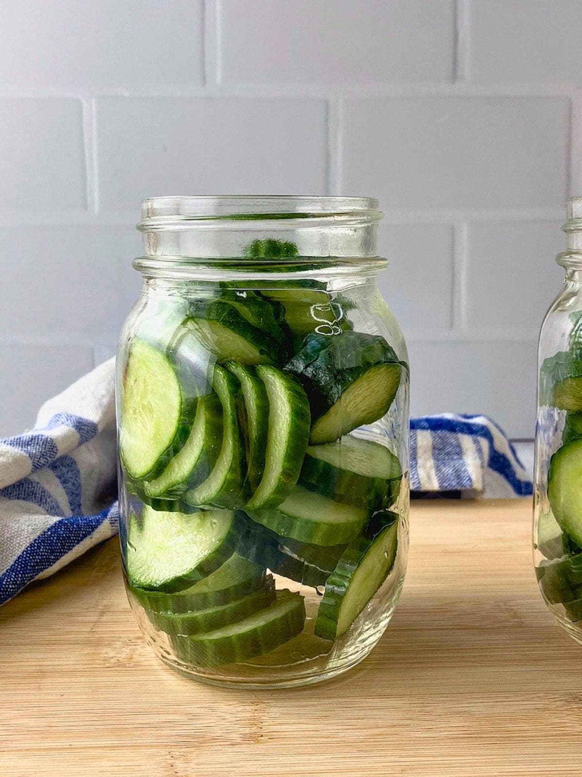 Pint sized glass jar filled with sliced cucumbers before the brine and spices are added.