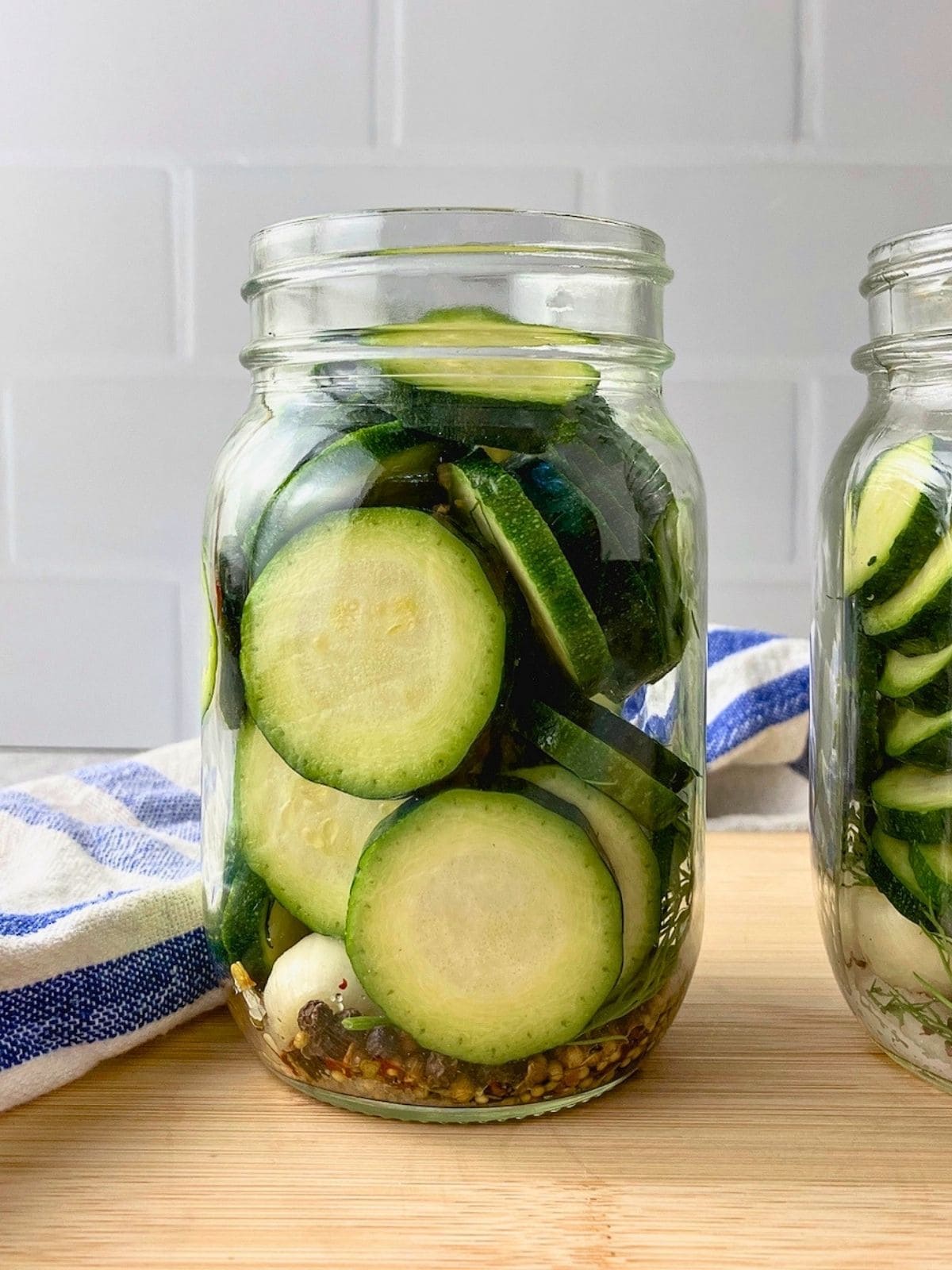 Pint sized jar filled with sliced zucchini, garlic, dill, peppercorns, pickling spice, and red pepper flakes for zucchini dill pickles before the brine is added.