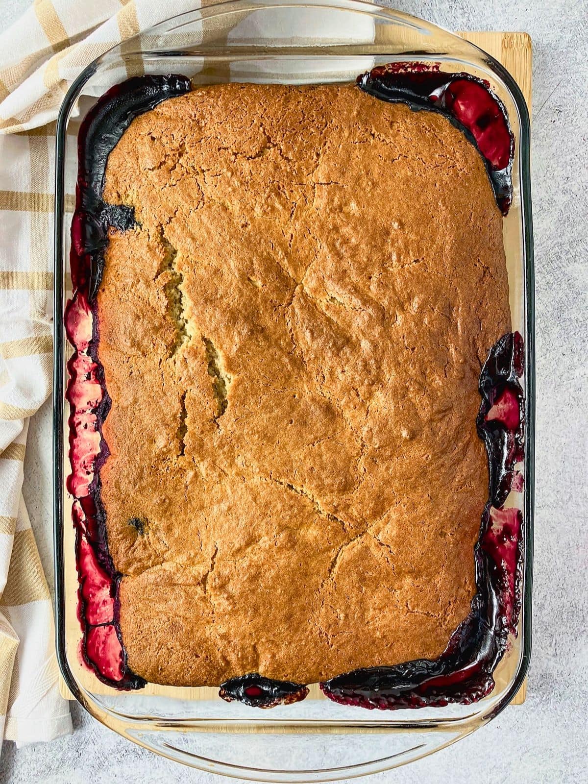 Baked blueberry cobbler in a glass dish with a golden cracked topping and dark blueberry filling bubbling around the edges.