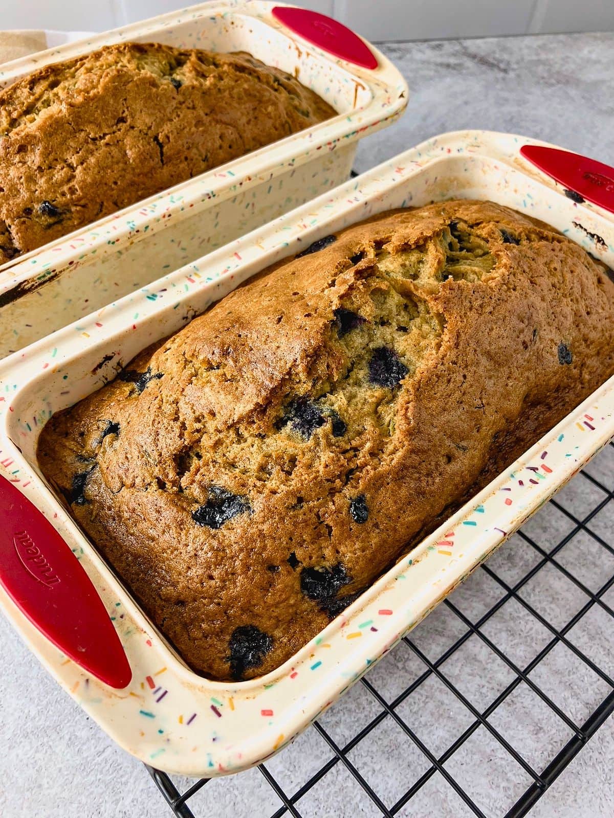 Two loaves of blueberry zucchini bread baked in loaf pans with golden domed tops and blueberries visible in the crust.