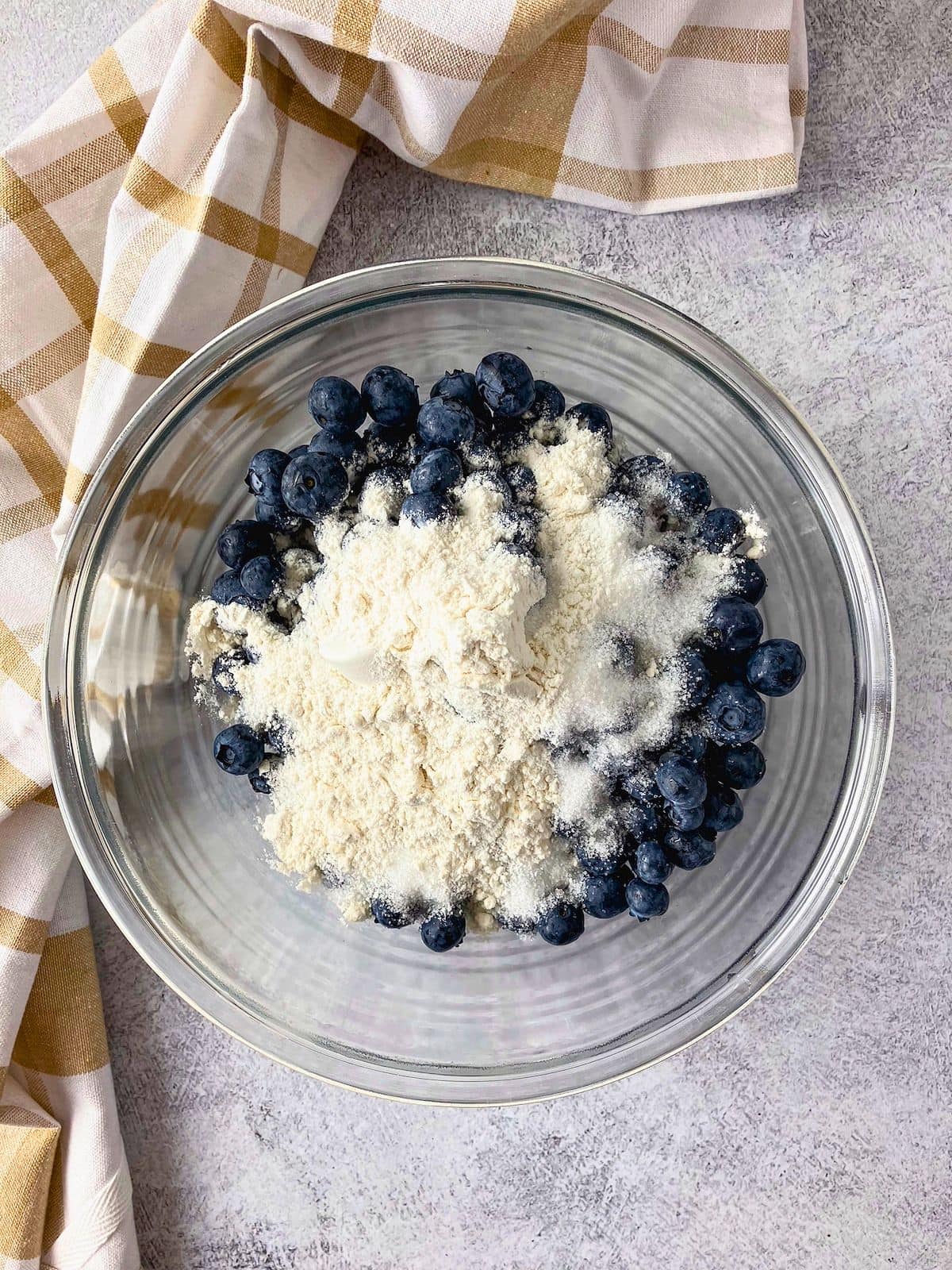Fresh blueberries covered with sugar and flour in a glass bowl for making blueberry cobbler filling.