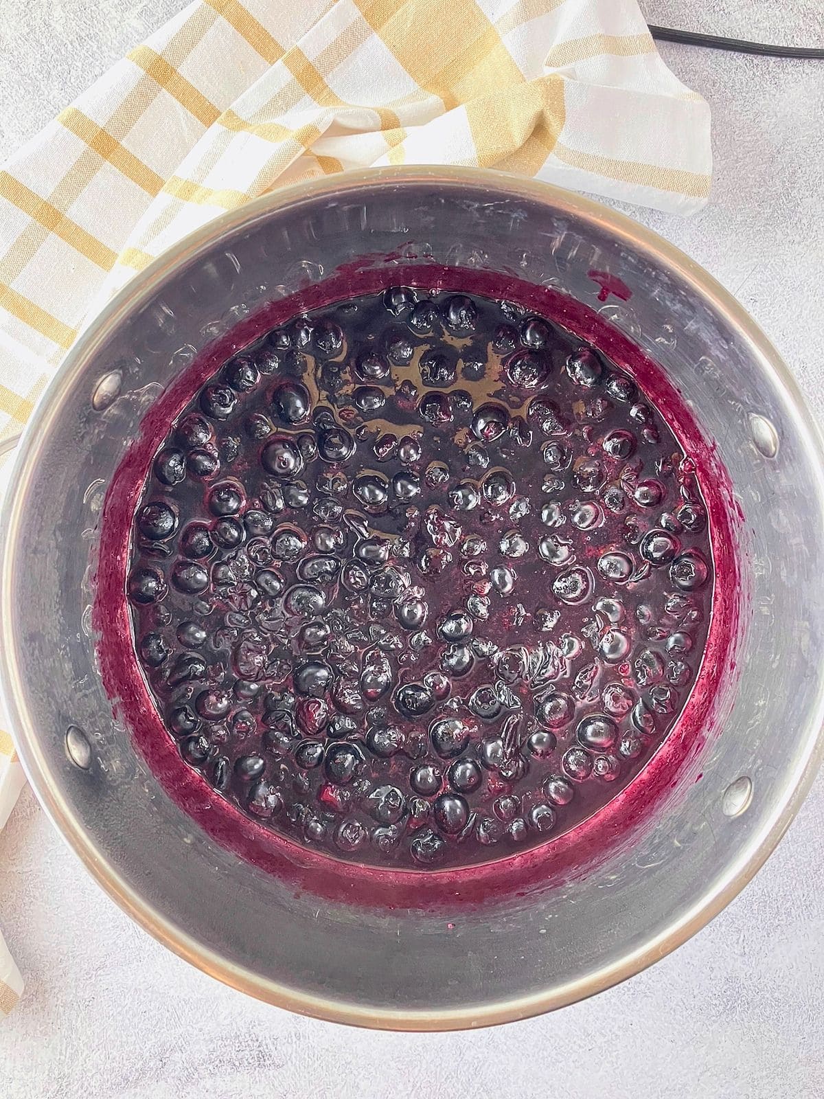 Blueberries simmering in a stainless steel pot with purple syrup coating the sides.