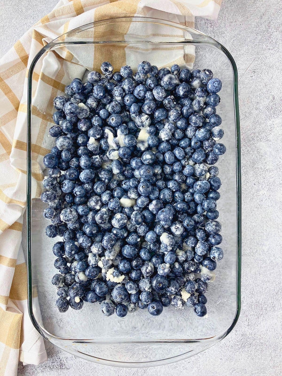 Blueberries tossed with sugar and flour in a glass baking dish for the filling layer of blueberry cobbler.
