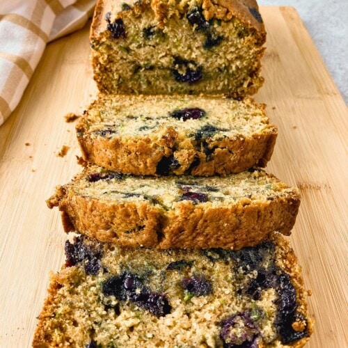 Sliced blueberry zucchini bread arranged on a cutting board with the remaining loaf behind it.